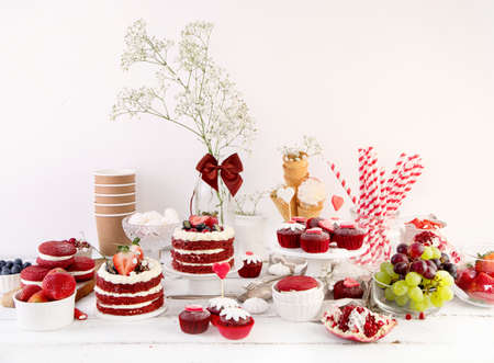 Delicious cake and cupcakes in red on white background. Table setting for celebration.の写真素材