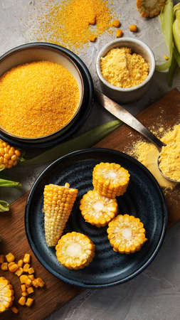 Corncobs and corn groats on gray background. Harvest food concept. Top view, flat lay, copy space