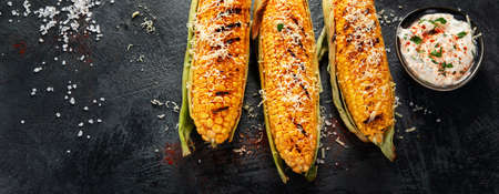 Grilled corncobs with cheese on dark background. Harvest food concept. Top view, flat lay, copy...