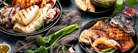 Grilled fish and seafood assortment on dark background. Homemade food concept. Panorama