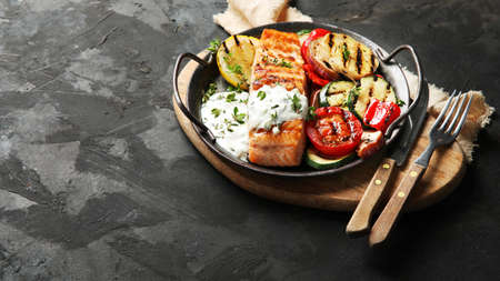 Salmon steak with vegetables and white sauce on dark background. Freshly grilled. healthy dinner....