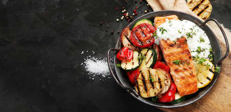 Salmon steak with vegetables and white sauce on dark background. Freshly grilled. healthy dinner. Mediterranean Diet. Top view, flat lay, copy spaceの写真素材