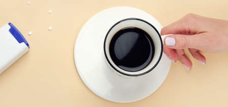 Close up of woman hand throwing saccharin pills in coffee cup on a white background, top view.の写真素材