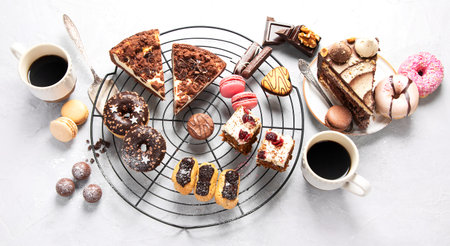 Table with various cookies, donuts, cakes and coffe cups on light backround. top view.