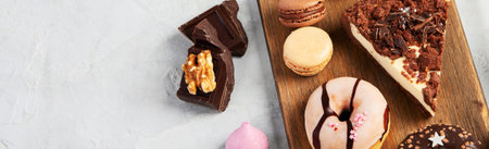 Selection of various cake pieces, macaroons, meringues, cookies and donuts on a wooden desk on a...