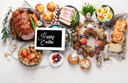 Traditional Easter dinner or brunch with ham, colored eggs, hot cross buns, cake and vegetables. Easter meal dishes with holday decorations. top view, copy spaceの写真素材