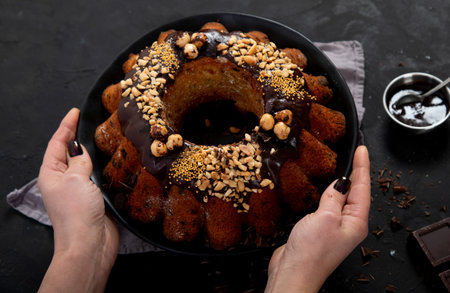 Bundt chocolate cake decorated with melted chocolate, nuts and sprinkles on plate on black...