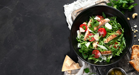 Chicken breast and fresh vegetable salad of lettuce, arugula, spinach, parmesan and tomatoes in dark plate. Healthy mediterranean dish. Keto diet eating. top view, copy spaceの写真素材