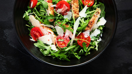 Chicken breast and fresh vegetable salad of lettuce, arugula, spinach, parmesan and tomatoes in dark plate. Healthy mediterranean dish. Keto diet eating. top viewの写真素材