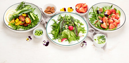 Delicious spring salads with edible flowers, vegetables, fruit, microgreens and cheese on a white background. Clean and healthy eating concept. top view. Panorama with copy space.の写真素材