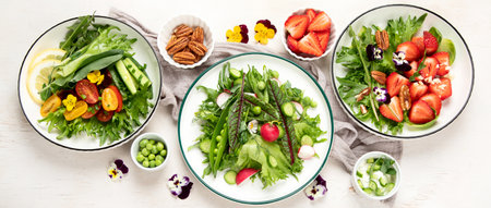 Delicious spring salads with edible flowers, vegetables, fruit, microgreens and cheese on a white background. Clean and healthy eating concept. top view. panorama.の写真素材
