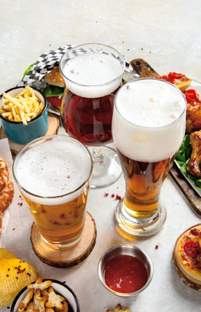 Fast food dish. Juicy burger, chicken wings, snacks, sauces and glasses of cold beer on light background. Top view.の写真素材