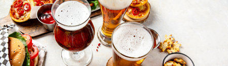 Fast food dish. Juicy burger, chicken wings, snacks, sauces and glasses of cold beer on light background. Top view.の写真素材