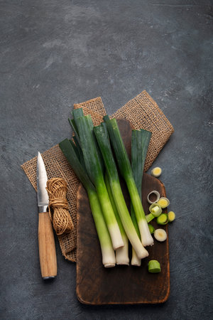 Whole and cut fresh leeks on a dark background, vegetarian food, healthy eating. Top view. Copy...