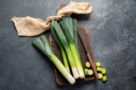 Whole and cut fresh leeks on a dark background, vegetarian food, healthy eating. Top view.