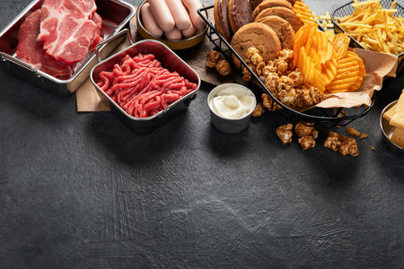 Saturated and trans. Unhealthy food. Sausage, potato, meat, cheese, popcorn, cookies, cream on dark background. Copy space.の写真素材