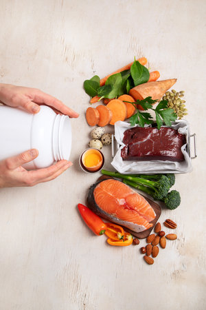 Vitamin A in food, natural products rich in vitamin A as red pepper, parsley leaves, dried apricots, carrots, broccoli, milk, egg yolk and cod liver oil on a light background. Top view.の写真素材