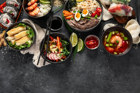 Traditional Asian food table. Spring roll, rice, shrimp, sushi, vegetables, meat on dark background. Top view, copy spaceの写真素材