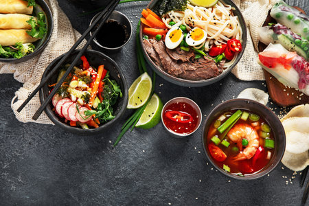 Traditional Asian food table. Spring roll, rice, shrimp, sushi, vegetables, meat on dark background. Top view, copy spaceの写真素材