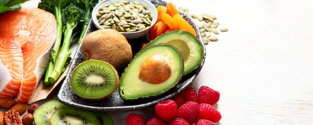 Foods rich in vitamin E such as dried apricots, hazelnuts, almonds, parsley leaves, avocado, walnuts, pumpkin seeds, sunflower seeds, spinach and fish on a white background. Top view. Panorama with copy space.の写真素材