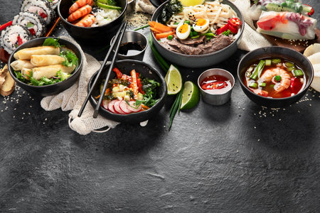 Traditional Asian food table. Spring roll, rice, shrimp, sushi, vegetables, meat on dark background. Copy spaceの写真素材