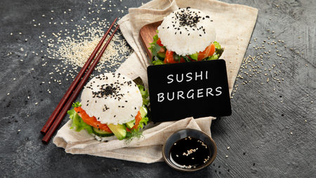 Asian sushi burger, soy sauce, chopstick on dark background. Trendy hybrid food.の写真素材