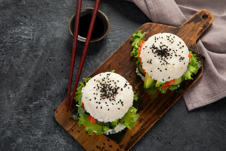 Asian sushi burger, soy sauce, chopstick on dark background. Trendy hybrid food. Top view, copy spaceの写真素材