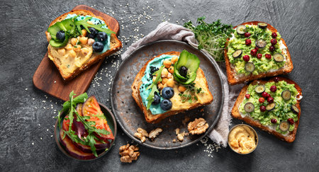 Vegetarian toasts with hummus, blueberry, avocado, tomato. delicious vegan breakfast on dark background. Top viewの写真素材