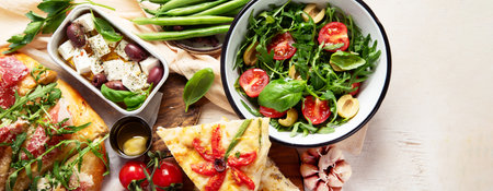 Full table of Italian meals on plates pizza, pasta, ravioli, salad and focaccia on white background....