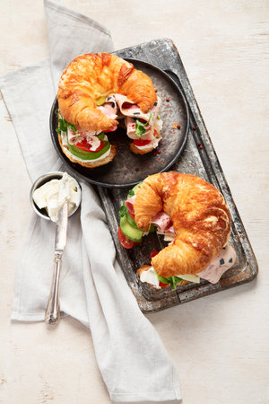 Salted healthy breakfast on light background. Fresh sandwich with croissant bun, cream cheese, avocado, ham. Top viewの写真素材