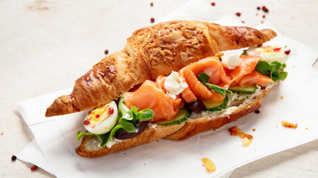 Salted healthy breakfast on light background. Fresh salmon croissant with cream cheese, cucumber, egg and salad.の写真素材