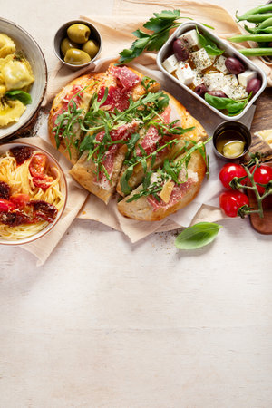 Full table of Italian meals on plates pizza, pasta, ravioli, salad and focaccia on white background. Top view. Copy space.の写真素材