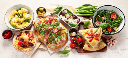 Full table of Italian meals on plates pizza, pasta, ravioli, salad and focaccia on white background. Top view. Panorama.の写真素材