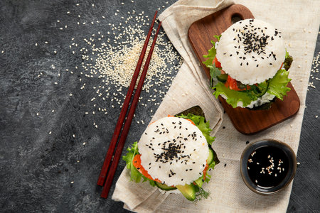 Asian sushi burger, soy sauce, chopstick on dark background. Trendy hybrid food. Top view, copy spaceの写真素材