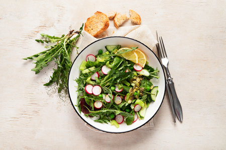 Spring vegan salad with dandelion leaves, radish, cucumber on wooden background. Top viewの写真素材