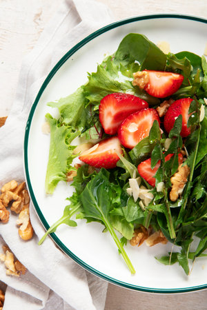 Dandelion salad with strawberry and wallnuts in plate on white background, top view.の写真素材