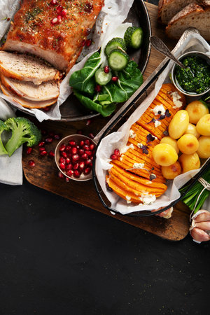 Roasted sliced ham with vegetables, bread and fresh salad on a black background. Top view. Copy space.の写真素材