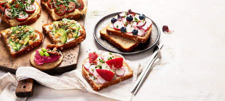 Various of vegan sandwiches on a light background. Healthy toasts with cheese, avocado, arugula, tomatoes and hummus. Healthy eating. Top view. Panorama with copy space.の写真素材