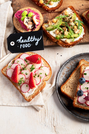 Various of vegan sandwiches on a light background. Healthy toasts with cheese, avocado, arugula, tomatoes and hummus. Healthy eating. Top view.の写真素材