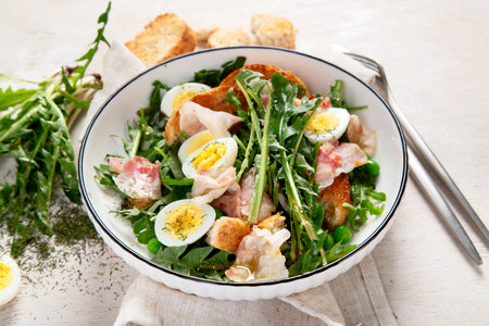 Summer fresh salad from dandelion leaves, eggs, bacon and with bread on light background. Top viewの写真素材
