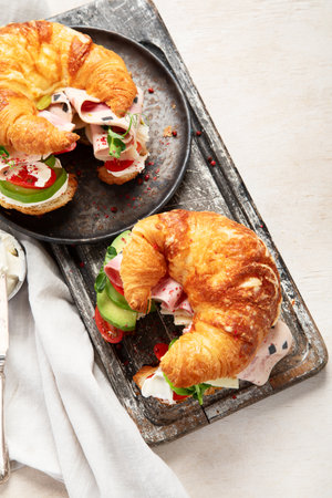 Salted healthy breakfast on light background. Fresh sandwich with croissant bun, cream cheese, avocado, ham. Top viewの写真素材