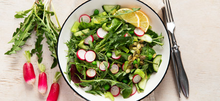 Spring vegan salad with dandelion leaves, radish, cucumber on wooden background. Top view, panoramaの写真素材