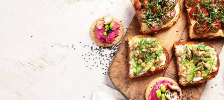 Various of vegan sandwiches on a light background. Healthy toasts with cheese, avocado, arugula, tomatoes and hummus. Healthy eating. Top view. Panorama with copy space.の写真素材