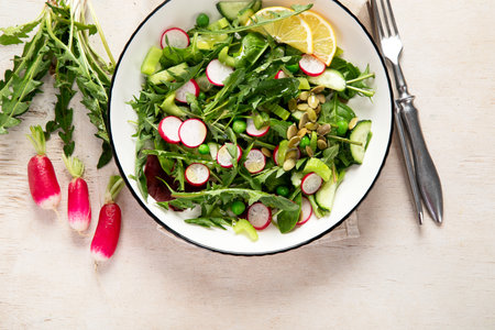 Spring vegan salad with dandelion leaves, radish, cucumber on wooden background. Top viewの写真素材