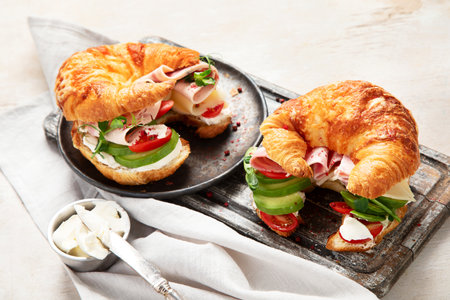 Salted healthy breakfast on light background. Fresh sandwich with croissant bun, cream cheese, avocado, ham.の写真素材