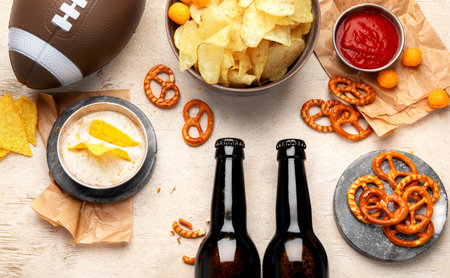 Snacks for watching an American football game. Beer, chips, pretzels, sauce on wooden background. Top viewの写真素材
