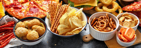 Large table of assorted take out food such as pizza, French fries, onion rings, burgers and snacks...