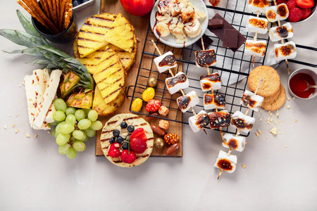Assortment of grilled sweets and fruits. Summer bbq table. Pineapple, peach, banana, marshmallow, strawberry, blueberry on light background. Top viewの写真素材