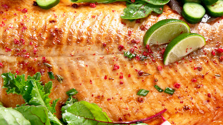 Cooked salmon with fresh greens and lime. Baked redfish on light wooden background. Top view