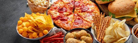 Large table of assorted take out food such as pizza, French fries, onion rings, burgers and snacks on a dark background. Top view. Panorama with copy space.の写真素材